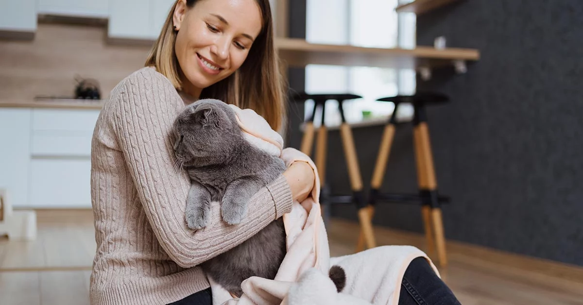 Belle femme jouant avec son chat et prenant soin de le couvrir dans une couverture et étreignant l'animal de compagnie à la maison