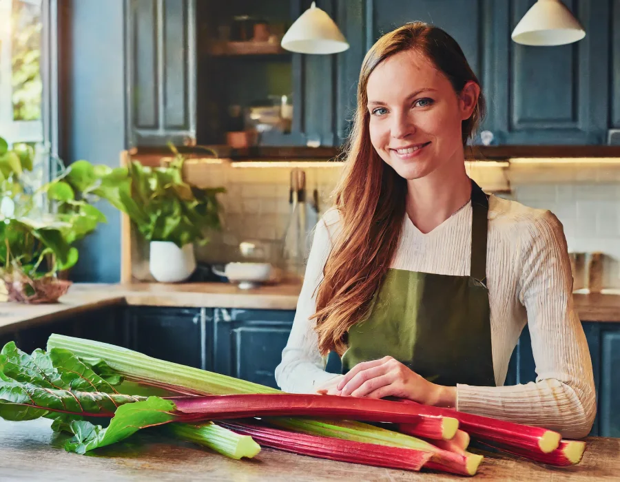 La Rhubarbe en Belle femme mince et souriante dans cuisine avec de la rhubarbe sur la table