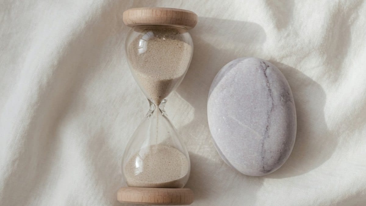 Sablier et galet posés sur un tissu en lin, symbole du temps calme accordé à la méditation