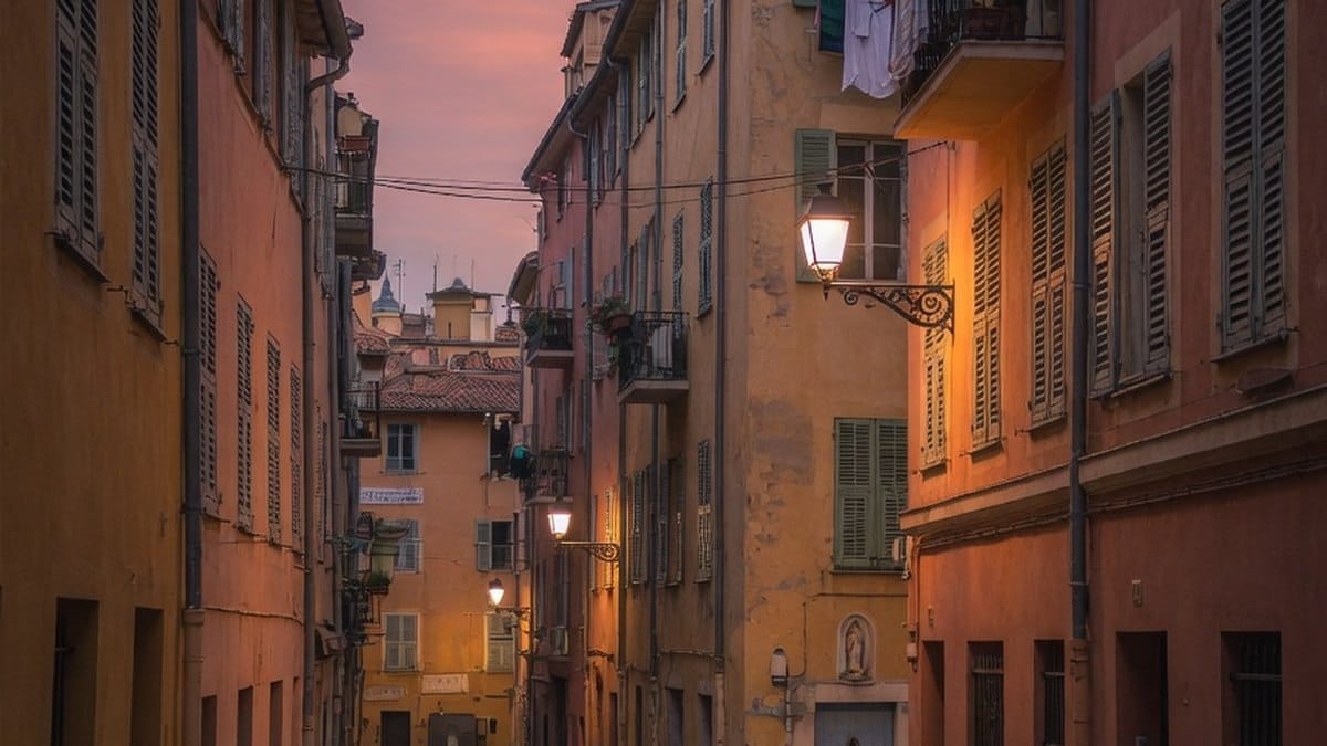 Rue étroite du Vieux-Nice au crépuscule, façades ocre et lampadaires allumés